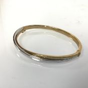 A 9ct yellow and white gold crossover stiff hollow hinged bangle (d.6.7cm x 5.5cm)