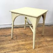 A Lloyd Loom style white painted garden table, the square top on an arched apron, with supports