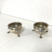 A pair of white metal cauldron style salts with flared scalloped rims, shell knees and hoof feet,