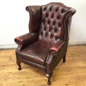 A George III style wing back armchair upholstered in deep plum hide, the arched back with buttoned