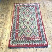 A hand knotted kelim rug, the field divided into lozenges, with serrated edges, within madder,