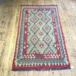 A hand knotted kelim rug, the field divided into lozenges, with serrated edges, within madder,