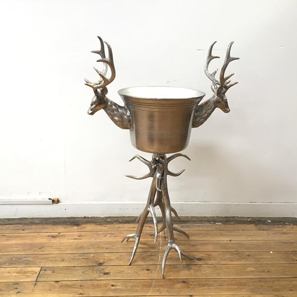 A handsome large metal wine bucket with silvered finish, flanked by two horned stags, on a support