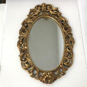 A modern oval wall mirror in gilt composition frame of interlocking C scrolls with a crown