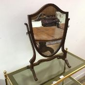 A 1920s mahogany swing mirror, the shield shaped glass within hinged frame, on scroll supports (58cm