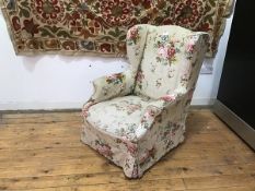 A wing back armchair in linen with floral upholstery, on square supports with castors (100cm x