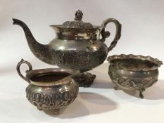 An Indian white metal three piece tea service comprising teapot with C scroll handle to side, with