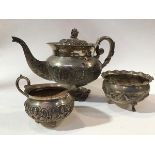 An Indian white metal three piece tea service comprising teapot with C scroll handle to side, with