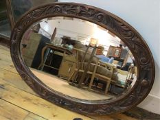 An Edwardian oak oval framed wall mirror with S scroll relief carved border and bevelled glass plate