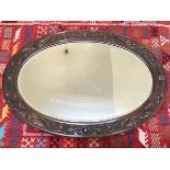 An Edwardian oak oval framed wall mirror with S scroll relief carved border and bevelled glass