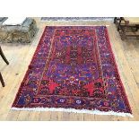 A hand knotted Hamadan rug, the red field with stylised woven flowerhead highlighted in blues and