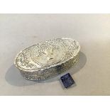 A Continental 800 standard oval chased pill box, with basket of flower and ribbon decorated top (