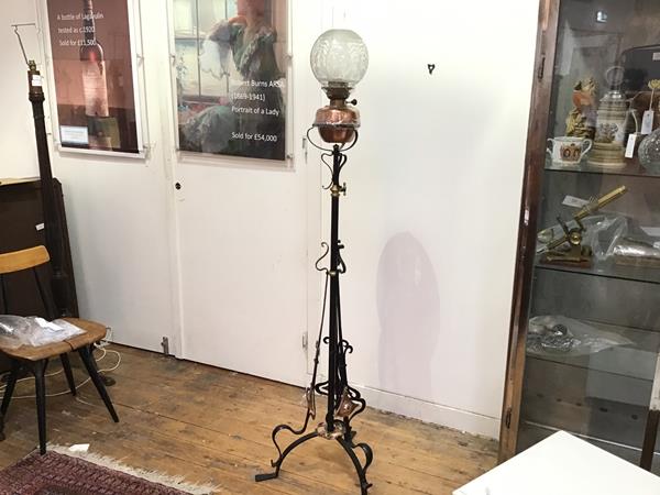 An Arts & Crafts wrought iron copper mounted stylised flowerhead tripod support oil lamp complete