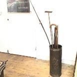 A embossed brass circular umbrella stand containing a collection of treen handled walking sticks,