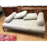 A modern daybed with mattress, two cushions and two bolsters, upholstered in a grey sand fabric,