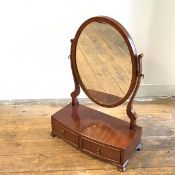 A reproduction mahogany bow fronted oval swing mirror raised on scroll end supports with bow fronted