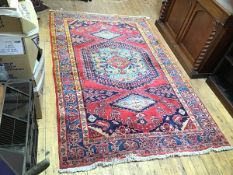 A handknotted rug, the red field with central medallion surrounded by a border of stylised