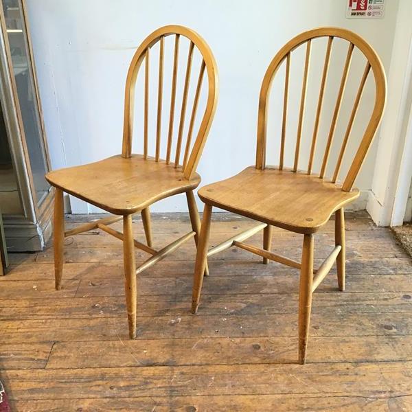 A pair of Ercol light ash spindle back kitchen chairs with shaped wood saddle seats, on turned