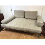 A large modern ottoman with two cushions and two bolsters, upholstered in a grey textured fabric, on