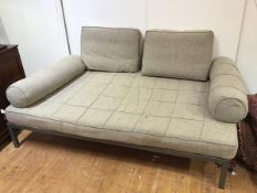 A large modern ottoman with two cushions and two bolsters, upholstered in a grey textured fabric, on