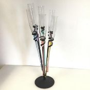 A novelty champagne flute stand with six flutes with elongated polychrome stems, lacking feet, in