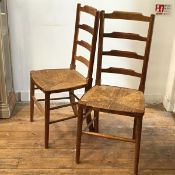 A pair of Edwardian oak ladderback rush seat bedroom chairs, raised on turned tapered supports