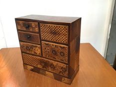 A 19thc Japanese hardwood straw decorated miniature cabinet, the top with inlaid design and an