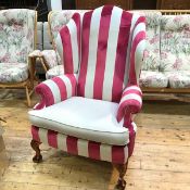A reproduction wing back easy chair, upholstered in striped cream and rose pink fabric, on carved