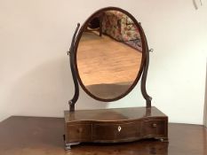 An early 19th century mahogany toilet mirror, the oval plate within scroll supports, on a serpentine