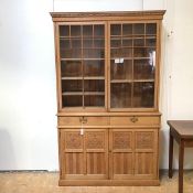 An arts and crafts oak bookcase, with dentil cornice above glazed doors with an arrangement of