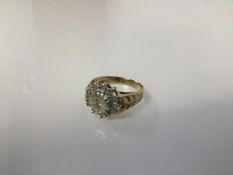 A 9ct gold diamond cluster ring in a flowerhead setting with leaf cast shoulders (O) (4.88g)