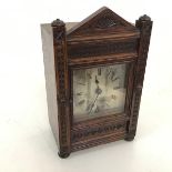 A 1920s oak mantel clock with carved architectural style facade, on bun feet, stamped John FB