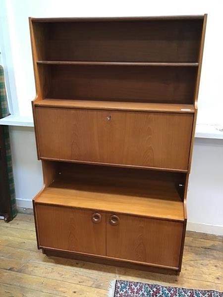 A mid century teak wall unit with two shelves above a fall front door, the base fitted a pair of