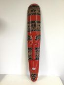 A Tribal mask of long slender form, painted red with further decoration (98cm x 18cm)