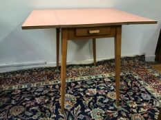 A 1960s/70s beech formica top kitchen table with fold up sides, fitted single frieze drawer, on