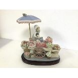 A Lladro figure of a Flower Seller and Cart (30cm x 26cm x 20cm), complete with stand