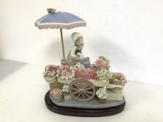 A Lladro figure of a Flower Seller and Cart (30cm x 26cm x 20cm), complete with stand