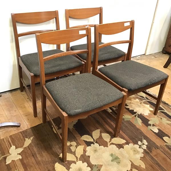 A set of four mid century teak chairs, with curved back rail above an upholstered seat, on