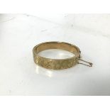 A 9ct gold bangle with clasp and safety chain, with foliate decoration to one side (6cm x 5.5cm) (