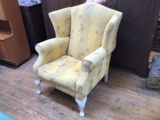 A wing back armchair in yellow foliate upholstery, on painted front cabriole legs (102cm x 90cm x