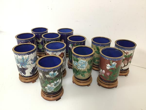 A set of twelve Chinese cloisonne beakers, with floral decoration, on wooden stands (each with