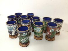 A set of twelve Chinese cloisonne beakers, with floral decoration, on wooden stands (each with