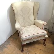 A modern Parker Knoll wing back armchair with foliate ivory upholstery, with burnt orange piping, on