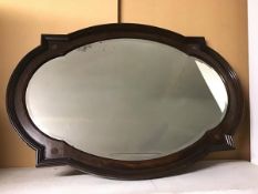 An Edwardian oak wall mirror, the bevelled glass within a barbed quatrefoil, with metal rosette to