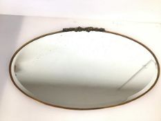 An Edwardian oval wall mirror with bevelled edge within a brass frame, with floral surmount (66cm