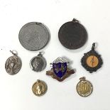 A collection of medals and charms, two gilt metal charms with religious themes, a Queen Victoria