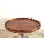 An oval wooden drinks tray with scalloped raised edge and brass handles to sides (57cm x 43cm)