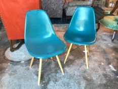 A pair of moulded plastic teal chairs on splay beech supports united by vertical X stretchers (
