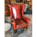A 1920s/30s wing back armchair in red leather with hump back on front turned supports united by X