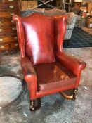 A 1920s/30s wing back armchair in red leather with hump back on front turned supports united by X